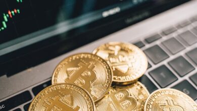 Close-up of gold Bitcoin coins on a laptop keyboard with a stock chart, symbolizing cryptocurrency market analysis.