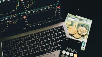 A laptop displaying stock charts with Bitcoin, Euros, and a cellphone calculator, showcasing financial analysis.