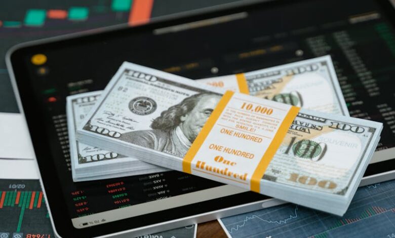 Stack of $100 bills placed on a tablet with financial graphs, symbolizing digital finance.