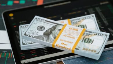 Stack of $100 bills placed on a tablet with financial graphs, symbolizing digital finance.