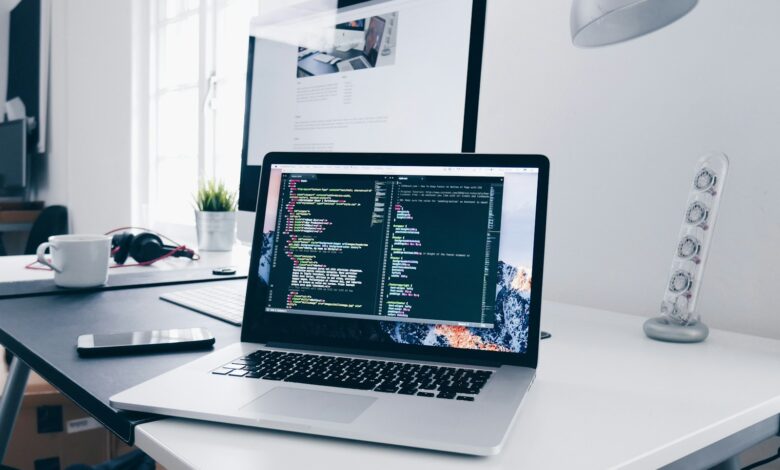 A MacBook with lines of code on its screen on a busy desk