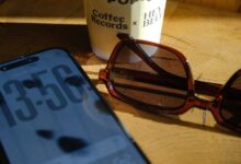 Smartphone, sunglasses, and coffee cup on wooden surface.