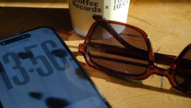 Smartphone, sunglasses, and coffee cup on wooden surface.