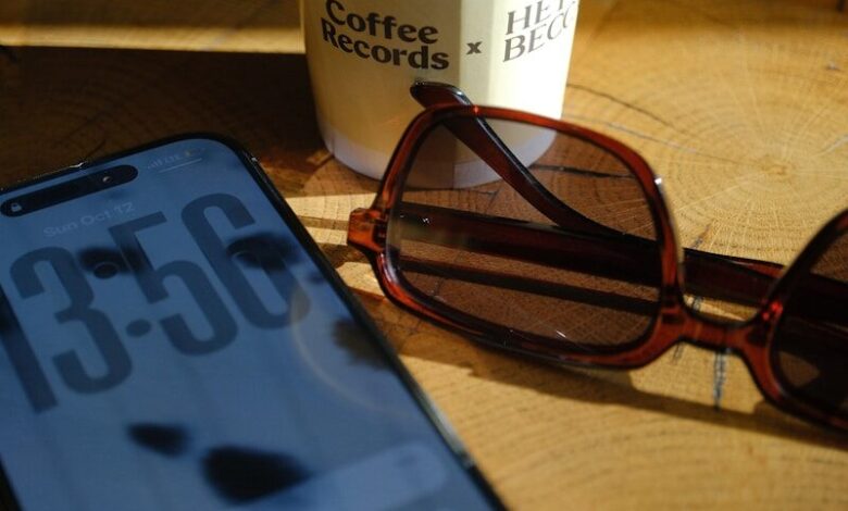 Smartphone, sunglasses, and coffee cup on wooden surface.